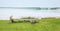 Peaceful scene of wooden bench for lying your back on the grass garden facing sandy beach with pigeon and seagull bird nearby.