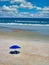 A peaceful and serene beach scene with sand, waves, clouds and umbrella