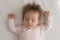 Peaceful sleepy baby girl lying on pale clean linen sheet