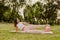 peaceful, smiling woman in pink clothes and small rubber ball doing pilates on pink mat at sunset in park in summer