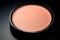 Peach fuzz color face powder in a black case on a black background without a lid. Copy space.