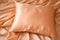 A peach fuzz color satin pillow on silky draped satin background