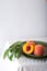 Peach in halves with bone in minimalistic style. Peaches with leaves on color green plate on table with white tablecloth. Ripe