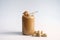 Peanuts butter in a clear glass bottle and pile of peanuts placed on white background.