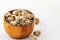 Peanuts covered with sesame seeds lies in a brown wooden bowl on a white wooden background
