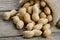 Peanuts in a miniature burlap bag on old, gray wooden surface