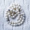 Pearl beads with strass inserts on a white lace knitted textile background are lined in a round curled shape.