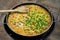 Peas and sweetcorn added to chicken paella in an outdoor pan