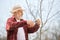 Peasant wearing panama hat cutting tree branches with pruner.