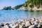 Pebble beach near Kalami with pine and cypress trees and an yacht at anchor in a bay on background. Corfu Island, Greece