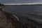 Pebbles shore of blue Lake Baikal, mountains on the horizon, clouds. Landscape