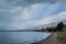 Pebbles shore with trees of clear calm undulating blue Lake Baikal, mountains on the horizon