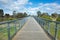 A pedestrian footbridge/boardwalk over wetlands leads to an Australian neighbourhood with some residential houses in the distance