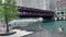 Pedestrians cross the riverwalk while el train passes overhead on the Chicago River during summer evening in Chicago Loop.