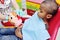 A pediatric dentist teaches an African American child who sits in a dental chair to brush his teeth properly.