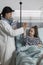 Pediatric expert doing high five gesture with ill kid sitting in patient bed