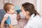 Pediatrician checking nose of baby girl with otoscope performing ENT exam at home during lockdown