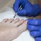The pedicurist covers the nails with pink varnish. Hands in blue gloves cares about a woman`s fo