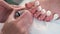 Pedicurist master is applying soft pink gel shellac on woman's toes, closeup.