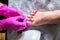 Pedicurist master in pink gloves cuts the cuticle and shellac toe nails in the pedicure salon using drill.  Professional pedicure