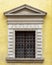 Pediment above a window of an ancient european house. Window with a wrought iron lattice.