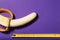 A peeled Banana is measured in length using a yellow ruler on a purple background