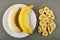 Peeled banana in plate, banana chips on gray table. Top view
