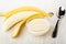 Peeled banana, spoon, transparent bowl with condensed milk on table