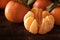 peeled clementine and whole fruits on a dark brown wooden board, close up