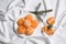 Peeled delicious ripe tangerines and fir branches on white bedsheet, flat lay