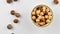 Peeled hazelnuts in a bowl and whole hazelnuts on a white background