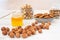 Peeled hazelnuts lie on a white table. Behind it is a small jar of honey, a rectangular gray bowl of peeled almonds, and two glass