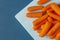 Peeled pieces of baby carrot on blue background. Flat lay. Copy space