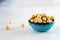 Peeled roasted hazelnuts in a blue round ceramic bowl stands on a white plate. Healthy and wholesome food high in protein.