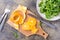 Peeled and sliced orange on a cutting board and a mix of arugula, chard and mizun on a plate on the table.