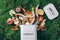 Peeled vegetables in white compost bin on green grass, moss background. Trash bin for composting with leftover from