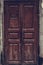 Peeling brown wooden door. Dilapidated wooden grunge door with cracked maroon paint. Threadbare dark red door.