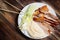 Peking Duck - Chinese roast duck with cucumber pieces, onion, pancakes on white plate close up. Wooden table and top view