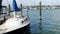 Pelican on a post near a sailboat tied to the dock in marina in with duck swimming in water behind the boat