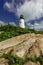 Pemaquid Point Lighthouse sits atop rugged rock layers on a bright summer day dotted with puffy clouds