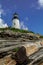 Pemaquid Point Lighthouse sits atop rugged rock layers on a bright summer day dotted with puffy clouds