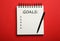 Pen and notebook with inscription GOALS on red background, top view. New Year aims