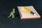 A pen, a spring-loaded notebook, and a miniature dinosaur against a black background. Small green figure of an animal of prey