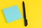 Pen with tack of sticky notes on solid yellow background with pink, yellow and blue on top with copy space for writing message