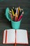 Pencil filled with colored pencils. In the form of a garbage container. Near an open notebook. Against the background of brushed