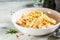Penne pasta with chicken, pepper and green onions in creamy sauce in a white plate, gray background