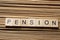 PENSION word written on wooden block at table.