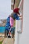 Pensioner washes the window,senior woman cleans and washes windows on a ladder from the street