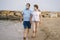 Pensioner woman and her husband taking romantic walk together - happy retired mature couple in face mask walking on the beach in