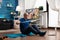 Pensioner working at body resistance exercising arms muscles using elastic band sitting on yoga mat